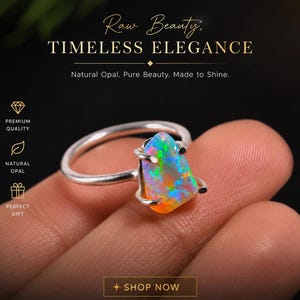 May include: A silver ring featuring a vibrant, multi-colored opal gemstone. The opal displays hues of blue, green, orange, and yellow. The ring is held in a hand, with text that reads "Raw Beauty, Timeless Elegance."