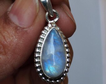 May include: A teardrop-shaped pendant with a polished, iridescent moonstone. The stone is set in a silver-colored metal with a beaded border and a small loop at the top for a chain. The moonstone displays a blue and white glow.