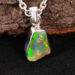 Puede incluir: Un collar con colgante de plata con una piedra de ópalo. El ópalo muestra tonos verdes, amarillos y rojos. El colgante está unido a una cadena de plata, creando una llamativa pieza de joyería.