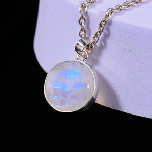 May include: A silver necklace featuring a round pendant with a moonstone. The moonstone has a white base with blue and iridescent highlights. The chain is a classic link style.