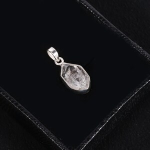 Pu&ograve; includere: Un pendente di cristallo trasparente e sfaccettato con un'ansa in argento. Il pendente &egrave; a forma di goccia e incastonato in una lunetta d'argento. Il cristallo presenta inclusioni interne e poggia su una superficie nera.