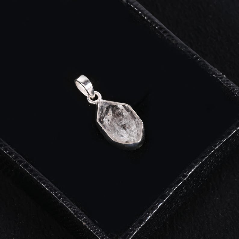 Pu&ograve; includere: Un pendente di cristallo trasparente e sfaccettato con un'ansa in argento. Il pendente &egrave; a forma di goccia e incastonato in una lunetta d'argento. Il cristallo presenta inclusioni interne e poggia su una superficie nera.