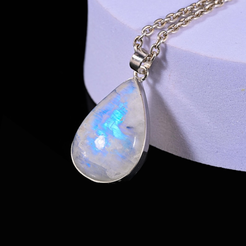 May include: A teardrop-shaped pendant necklace with a silver chain. The pendant features a large, iridescent moonstone with blue and white hues. The stone is set in a silver bezel.