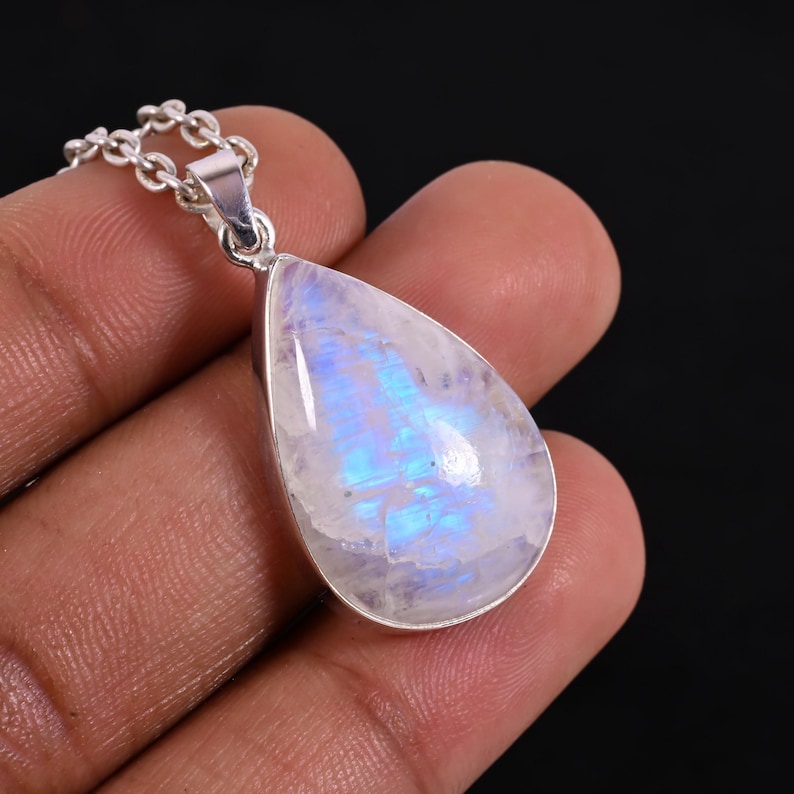 May include: A teardrop-shaped moonstone pendant necklace. The iridescent stone has a pearlescent white base with blue and purple flashes. The pendant is set in a silver-colored metal and hangs from a delicate chain.