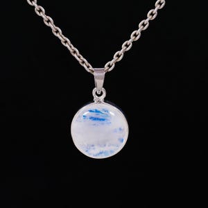 May include: A silver necklace with a round pendant. The pendant features a white and blue stone, set in a silver bezel. The chain is a classic link style, and the background is black.