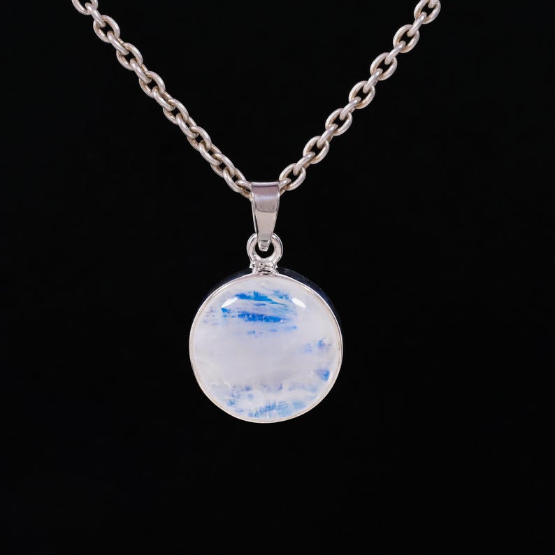 May include: A silver necklace with a round pendant. The pendant features a white and blue stone, set in a silver bezel. The chain is a classic link style, and the background is black.