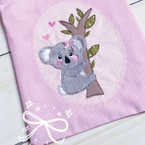 Może przedstawiać: Różowa torba z tkaniny z aplikacją koali na drzewie z różowymi sercami. Torba ma różowo-biały wzór kwiatowy na górze i różowy wzór w kropki na dole.