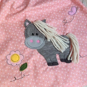 May include: A pink dress with a white polka dot pattern featuring an embroidered grey horse with a white mane and tail, a yellow flower, and a pink butterfly.
