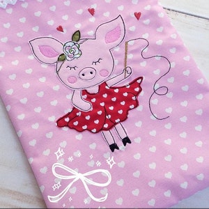 Op de afbeelding: Roze stof met een wit hartpatroon en een witte kantbies. Een roze varken dat een rode jurk met witte hartjes draagt, is geborduurd op de stof. Het varken houdt een stok vast met een touwtje eraan.