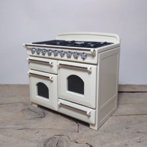 Puede incluir: Una cocina blanca independiente con una parte superior negra y botones plateados. La cocina tiene dos hornos con puertas de vidrio y manijas plateadas.