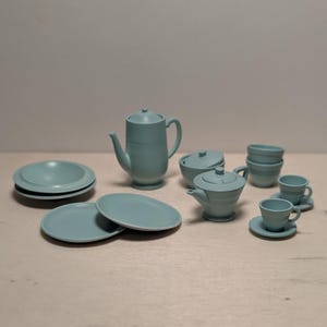 Könnte beinhalten: Ein mattes, hellblaues Teeservice bestehend aus einer hohen Teekanne, einer kleineren Teekanne mit Deckel, einer Zuckerdose mit Deckel, zwei gestapelten Tellern, zwei einzelnen Tellern, zwei gestapelten Schalen und zwei Tassen mit passenden Untertassen.