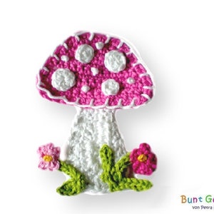 Könnte beinhalten: Ein rosa-weißer gehäkelter Pilz mit weißen Punkten und grünen Blättern. Der Pilz sitzt auf einem weißen Hintergrund.