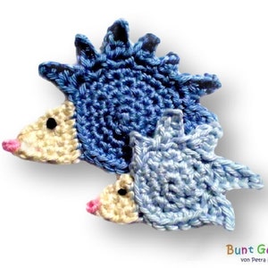 Peut inclure: Deux hérissons en crochet, l'un bleu et l'autre bleu clair, avec des nez roses. Le plus grand hérisson est assis sur le plus petit.