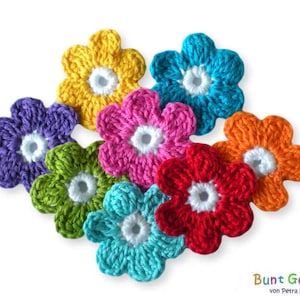 Könnte beinhalten: Sieben gehäkelte Blumen in verschiedenen Farben, darunter lila, grün, rosa, rot, orange, gelb und blau. Jede Blume hat eine weiße Mitte.