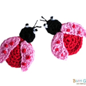 May include: Two crocheted ladybug ornaments with pink wings and black heads. The ladybugs have red spots on their wings.