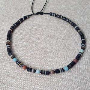 Peut inclure: Un collier de perles noires avec une variété de perles colorées, notamment turquoise, rouge et marron. Le collier est composé de petites perles rondes et est enfilé sur un cordon noir.
