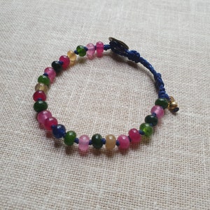 May include: A blue cord bracelet with a silver clasp and multi-colored beads. The beads are pink, green, and blue.