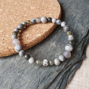 Può includere: Un braccialetto di perline grigio e bianco con un mix di perline grigio chiaro, grigio scuro e nero. Il braccialetto è fatto di pietre naturali e ha un design semplice ed elegante.