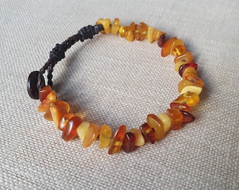 Könnte beinhalten: Ein Armband aus polierten Bernsteinen in Gelb-, Orange- und Brauntönen. Die Steine sind auf einem dunkelbraunen Kordelband aufgefädelt, das mit einem Knopf verschlossen wird. Das Armband ist etwa 18 cm lang.
