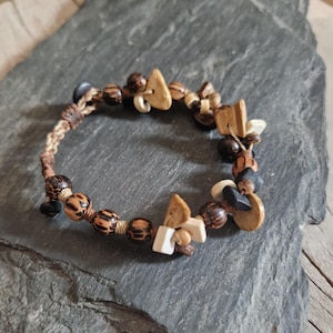 Peut inclure: Un bracelet artisanal composé de perles en bois, de pierres naturelles et de formes géométriques en bois. Le bracelet présente des nuances de marron, beige et noir, assemblées sur un cordon tressé. Le design a une esthétique rustique et bohème.