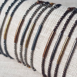 May include: A collection of beaded bracelets with different colored accents. The bracelets are made with small, round beads in silver, gold, and copper tones. The accents are made with longer, rectangular beads in black, gold, and copper tones.