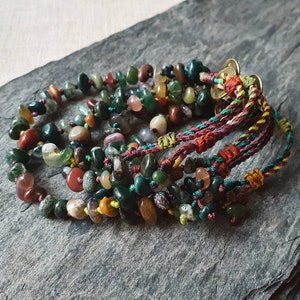 Può includere: Un set di braccialetti multicolori realizzati con piccole pietre di forma irregolare e cordini intrecciati. Le pietre sono di colore verde, marrone, rosso e arancione. I cordini sono rossi, verdi e gialli.