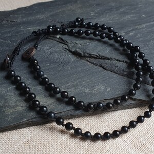 Op de afbeelding: Een zwarte kralenketting met een zwart koord en een houten knoopsluiting.