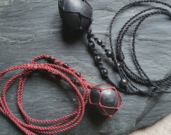 May include: Two black stone pendants with a geometric pattern, each hanging from a cord. One cord is black and the other is burgundy.