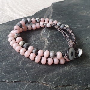 May include: A double-strand bracelet with pink and gray beads and a brown cord with a black button closure.