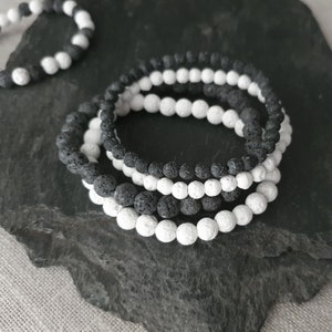 May include: Four stacked bracelets made of black and white lava rock beads. The bracelets are on a dark gray background.