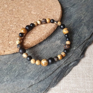 Può includere: Un braccialetto con perline marroni e nere. Il braccialetto è realizzato con materiali naturali e ha un design semplice ed elegante.