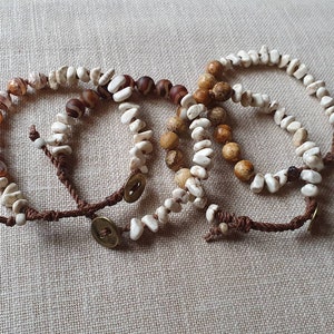 Op de afbeelding: Drie kralenarmbanden met bruine, witte en bruine stenen. Elke armband heeft een bruin koord met een metalen knoopsluiting.