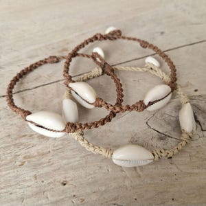 Bracciale con conchiglie di ciprea, con conchiglia forata fissa e cordino intrecciato, disponibile in 5 colori (1/2/3 conchiglie), chiusura con bottone turchese e bianco personalizzabile.