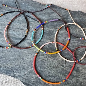Può includere: Cinque braccialetti colorati con perline e chiusure regolabili in corda. I braccialetti presentano una varietà di colori, tra cui nero, marrone, arancione, giallo, rosa, blu, rosso e bianco.