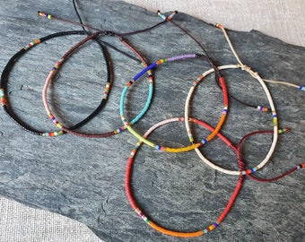 May include: Five colorful beaded bracelets with adjustable string closures. The bracelets feature a variety of colors, including black, brown, orange, yellow, pink, blue, red, and white.