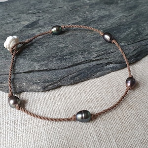 Può includere: Una collana di corda marrone con cinque perle verde scuro. La collana ha una chiusura a levetta bianca.