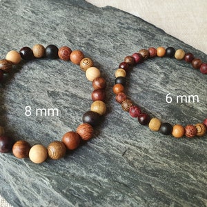 May include: Two wooden bead bracelets, one with 8 mm beads and the other with 6 mm beads. The bracelets are made from different types of wood, including brown, red, and natural wood.
