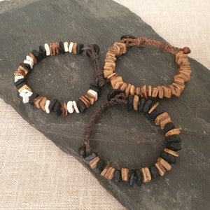 以下が含まれることがあります： 茶色、黒、白のビーズが付いた木製ブレスレット3本。ブレスレットは茶色の紐で結ばれています。