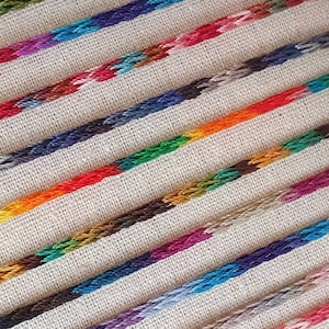 Puede incluir: Primer plano de una variedad de carretes de hilo de bordar de colores dispuestos en filas sobre un fondo de tela blanca.