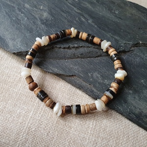 Op de afbeelding: Een bruin, zwart en wit kralenarmband met witte schelpaccenten.