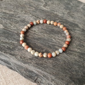 Op de afbeelding: Een kralenarmband met bruine, beige en witte stenen.