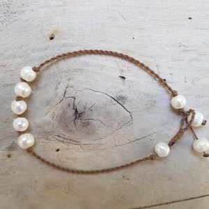 Op de afbeelding: Een bruine koordketting met witte parel kralen. De ketting is aan de achterkant met een knoop vastgemaakt.