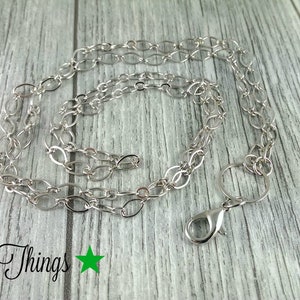 Könnte beinhalten: Silberkette mit einem Karabinerverschluss, 80 cm lang. Die Kette besteht aus ovalen Gliedern.