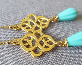 Pendientes largos, elegantes con ornamento de color dorado y cuentas de bohemia en forma de gotas color turquesa. Estilo boho chic.