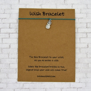 May include: A brown card with the text "Wish Bracelet" printed in black. The card has a teal string with a silver pineapple charm attached. The text on the card reads: "Tie this Bracelet to your wrist, as you do make a wish. When the bracelet breaks in two, legend says your wish will come true! salemwishes.com"