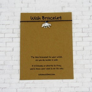 May include: A brown card with the text "Wish Bracelet" printed on it. The card has a black string with a silver charm of a bear attached to it. The text on the card reads: "Tie this bracelet to your wrist, as you do, make a wish. If it breaks or starts to fray, you'll know your wish is on its way. salemwishes.com"