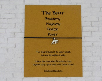 Puede incluir: Una tarjeta marrón con las palabras "The Bear" y una lista de palabras: Bravery, Majesty, Peace, Power. La tarjeta tiene una cuerda negra con un dije de oso plateado. El texto en la tarjeta dice: "Ata este brazalete a tu muñeca, cuando hagas un deseo. Cuando el brazalete se rompa en dos, la leyenda dice que tu deseo se hará realidad! salemwishes.com"