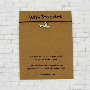 May include: A brown card with the text "Wish Bracelet" printed on it. The card has a black string with a silver shark charm attached to it. The text on the card reads: "Tie this Bracelet to your wrist, as you do make a wish. When the bracelet breaks in two, legend says your wish will come true! salemwishes.com"