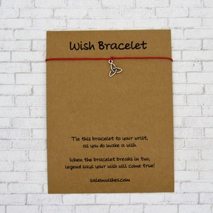 May include: A red string bracelet with a silver Celtic knot charm. The card reads "Wish Bracelet" and includes instructions on how to make a wish and the legend associated with the bracelet. The card also includes the website salemwishes.com.