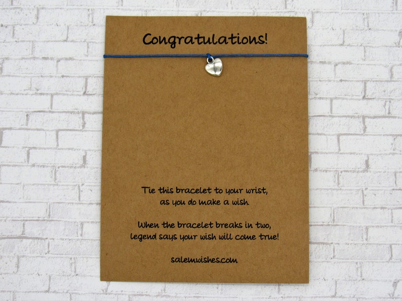 May include: A brown card with the text "Congratulations!" printed on it. The card has a blue string with a silver heart charm attached to it. The text on the card reads: "Tie this bracelet to your wrist, as you do make a wish. When the bracelet breaks in two, legend says your wish will come true! salemwishes.com"